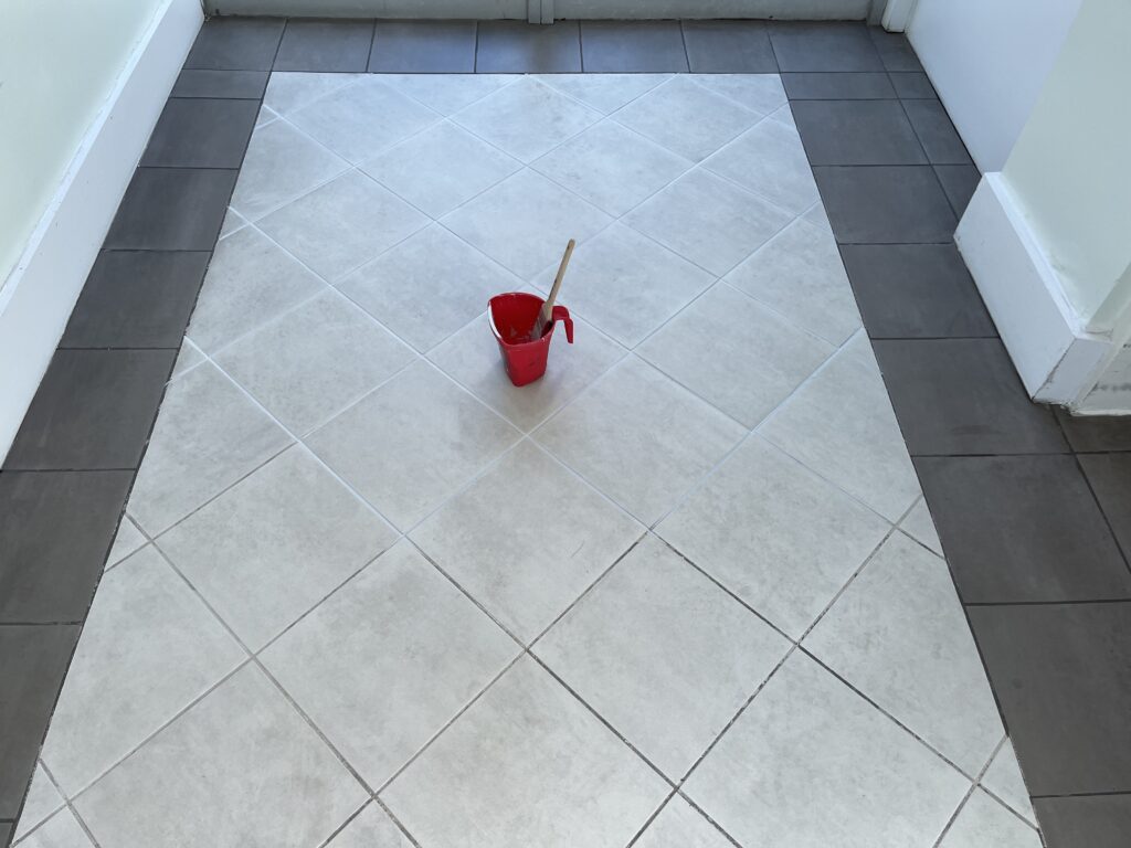 Grout color sealing in a Plantation home showing half-painted grout lines with red cup during floor transformation process